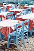 Tische mit rot-weiss karierten Tischdecken und pastellblauen Binsenstühlen in einer griechischen Taverne am Meer