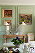 Console with candlesticks and table lamps, painting on green wall in living room