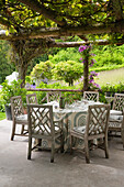 Round table with patterned tablecloth under overgrown pergola in garden