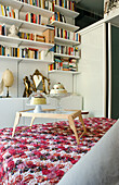 Modern bedroom with wall shelf, floral bedspread and small wooden table with biscuits