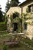 Stone house with rose garland and wooden deckchairs in the garden