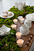Desserttisch, dekoriert mit Frühblühern und Moosen mit Makronen, Kerzen und weißem Geschirr