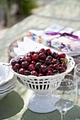 Cherries in white china pedestal dish and wine glasses on table
