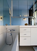 Modern bathroom with bathtub next to white washstand below large mirror on wall