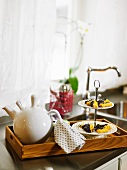 A teapot and biscuits on a wooden tray in a kitchen