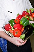 A chef holding a tray of fresh vegetables