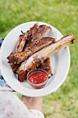 person holding a plate of grilled spare ribs and barbecue sauce