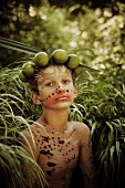 Junge mit Limettenkrone, als Wald-Nymphe geschminkt, im hohen Gras