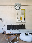 Loftartiger Wohnraum mit Bauhaus Hängelampe über Sessel und Polster-Couchtisch vor Sofa