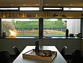 Dining area in front of modern kitchen counter below large windows with view of garden