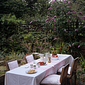Gedeckter Tisch im Garten vor Backsteinmauer mit üppiger Vegetation