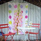 Bunter Sitzbereich mit roten Stühlen und Blumenposter im Garten