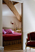 View of cosy bedroom with exposed wooden beams and red armchair