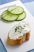 Sliced cucumbers and a baguette topped with cream cheese and chives