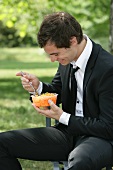 Mann isst geraspelte Möhren auf einer Parkbank