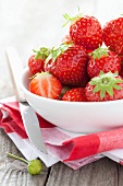 Fresh strawberries in a bowl and fruit knife on tea towel
