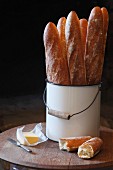 Baguettes in bucket and butter on wooden board