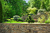 Well-kept garden with natural stone wall and various deciduous trees