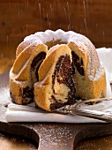 Dusting a vanilla and chocolate bundt cake with icing sugar