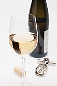 A glass of white wine, cork, corkscrew and bottle of white wine