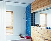 Simple bathroom with coloured tiles above bathtub and mirror in niche of wood-clad wall