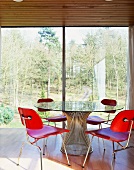 Wooden chairs stained red at glass table in front of floor-to-ceiling terrace doors with a view