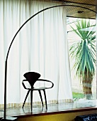 Fifties-style wooden chair in front of half-closed curtain at window and view of yucca