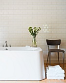Chair next to free-standing bathtub in front of white tiled wall