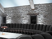 Curved black leather couch in front of illuminated stone wall