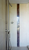 Um eine Stufe versenkte Dusche mit Designer Armatur und senkrechter Fliesenbordüre aus dunklem Marmor
