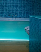 Bathtub with indirect lighting in bathroom with blue mosaic tiles