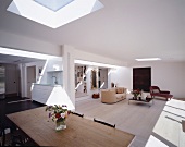 Large, open-plan living space with sunny skylights above seating area, dining table and kitchen unit