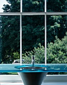 Designer washstand with blue glass slab in front of lattice window with view of trees