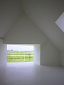 Moderner, leerer Dachraum mit rahmenlos verglaster Wandöffnung und Blick in Landschaft