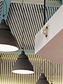 Grey, metal, industrial-style pendant lamps in front of white slatted cladding