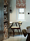 Integriertes Brennholzregal neben Schreibtischecke mit Designerstuhl und floral gemustertem Faltrollo