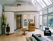 Collection of furniture and ornaments in high, open-plan living space with conservatory glazing and rounded gallery