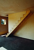 Simple wooden staircase without balustrade and sunlight falling on concrete floor in wooden house with plywood cladding
