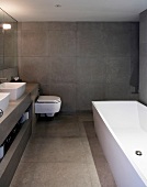 Bathroom tiled in grey with bathtub, washstands & toilet
