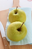 Two apples on a chopping board with a knife