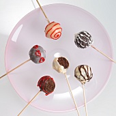 Cake pops with chocolate icing and red writing icing, one with a bite taken out