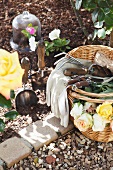 Korb mit Rosen und verschiedenen Gartenutensilien neben einem Blumenbeet