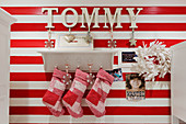 Christmas stockings hanging from traditional bracket shelf on red and white striped wall