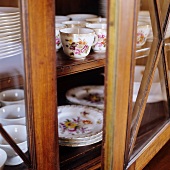 Display cabinet with slightly open door and view of floral tea service