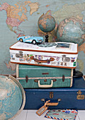 Stack of vintage suitcases, tin toy car and globes in front of a map