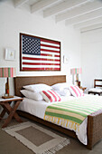 Bedroom with rattan bed, striped bed linen and American flag as wall decoration