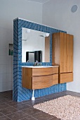 Minimalist vanity and wooden cupboard on a blue, mosaic tile dividing wall in a bathroom