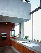 Kitchen counter in front of glass wall beneath floating concrete gallery