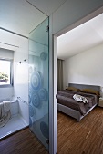 Blick ins moderne Schlafzimmer und Bad Ensuite mit Stäbchenparkett und Glastür