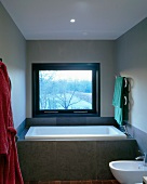 Vor Fenster eingebaute Badewanne mit grauer Fliesenverkleidung